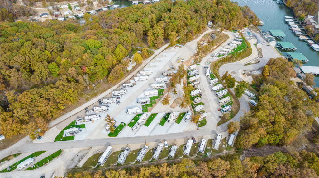 Aerial view of a scenic RV park surrounded by lush, colorful trees near a calm water body with boat docks.