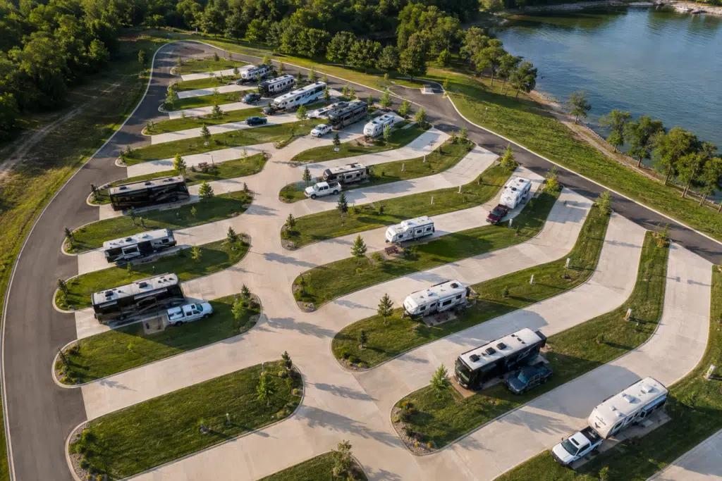 Aerial view of pull-through RV sites beside a lake, with a mix of empty sites and occupied sites featuring RVs and vehicles.